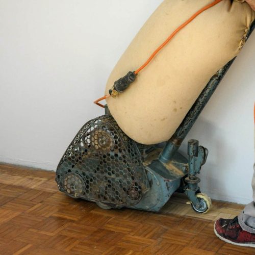 Close-up photo of man sanding hardwood floor with grinding machine