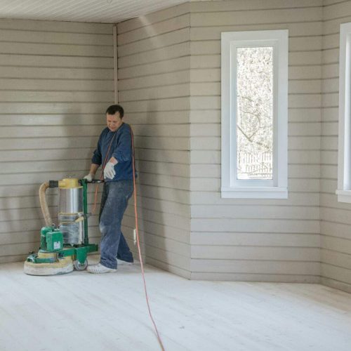 Man grinding floors with a grinder in a wooden house.