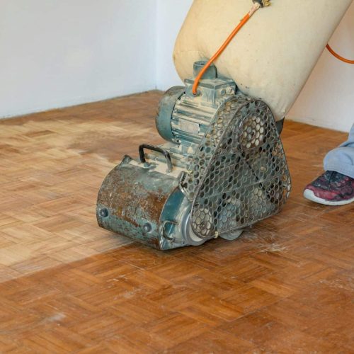 Man sanding hardwood floor with grinding machine