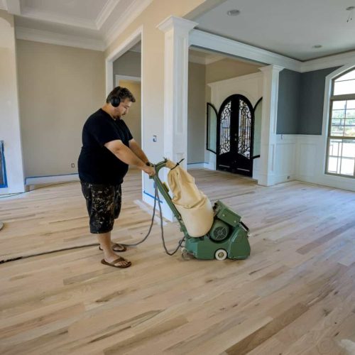 The process grinding a wooden parquet floor in using floor sander of newly constructed house