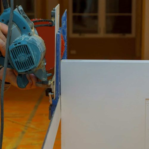 Wood siding contractor using an electric compound miter saw to cut door trim boards in the construct