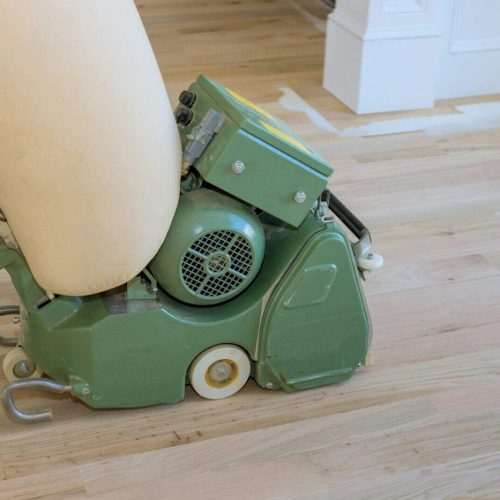 Wooden parquet floor being ground by carpenter using floor sander in a newly constructed home