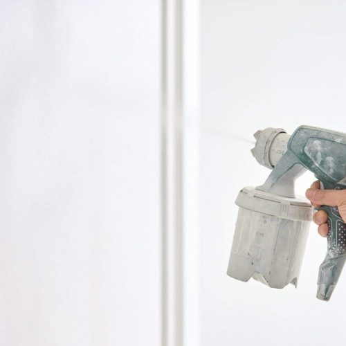Worker painting wall with spray gun in white color.