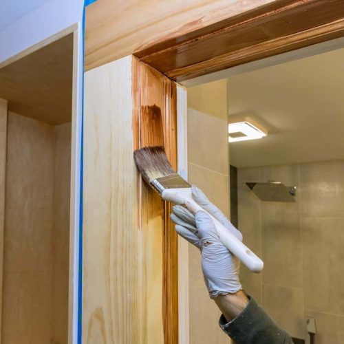Worker uses brush to paint wooden door frames molding with a stain